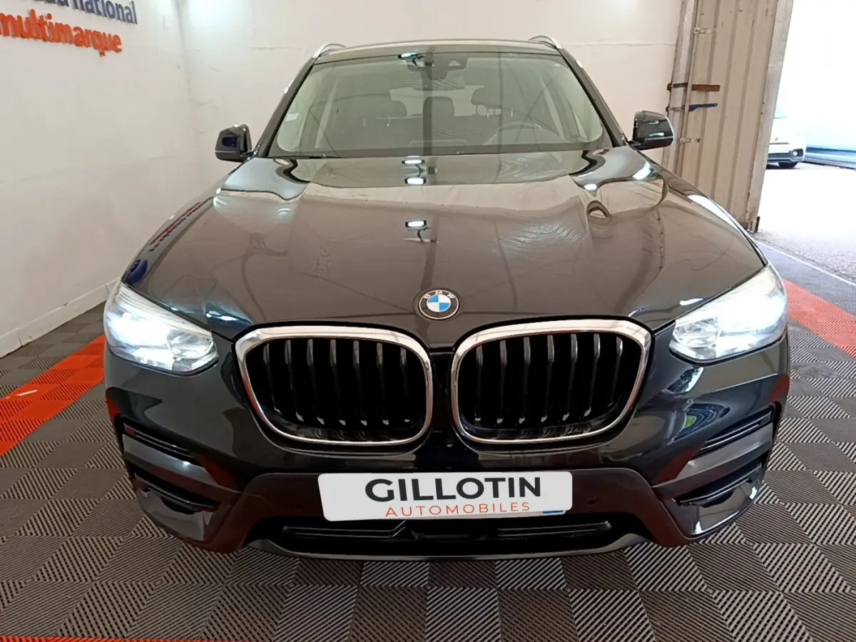 BMW X3 xDrive20d noir vu de face avec calandre double haricot et phares LED allumés dans un showroom.