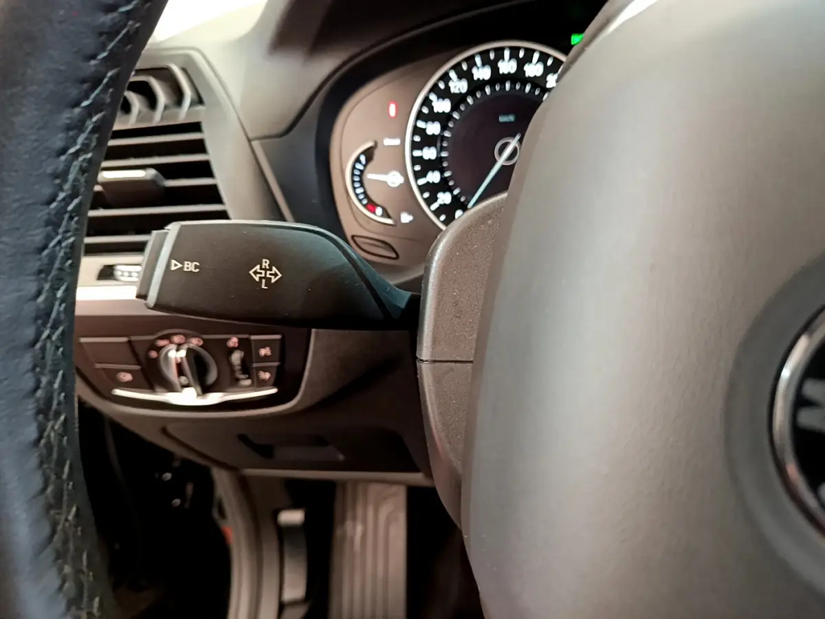 Gros plan sur la manette de commande à gauche du volant du BMW X3 noir, avec tableau de bord et compteurs visibles.