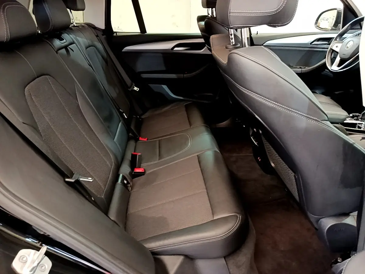 Vue intérieure arrière du BMW X3 noir 2020, sièges en cuir et tissu avec surpiqûres blanches visibles.