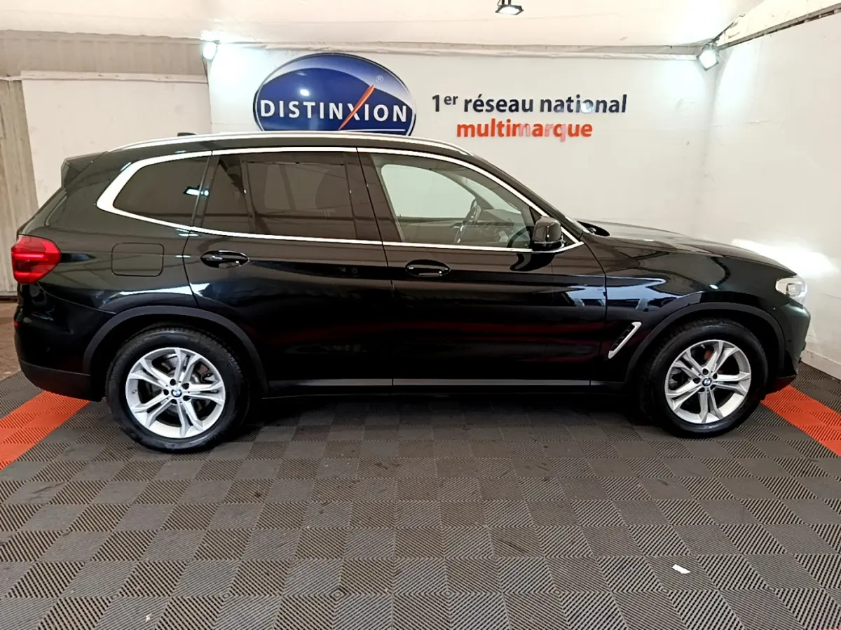 Profil côté droit d'un BMW X3 noir 2020, avec jantes alliage et vitres teintées, stationné en intérieur showroom.