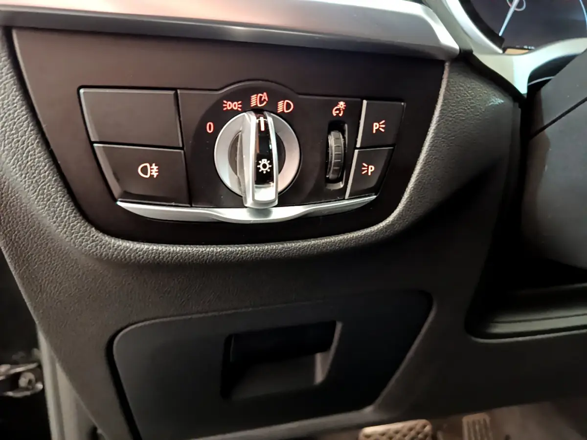 Gros plan sur le panneau de commande des phares du BMW X3 xDrive20d 2020, intérieur noir avec commandes rétroéclairées rouges