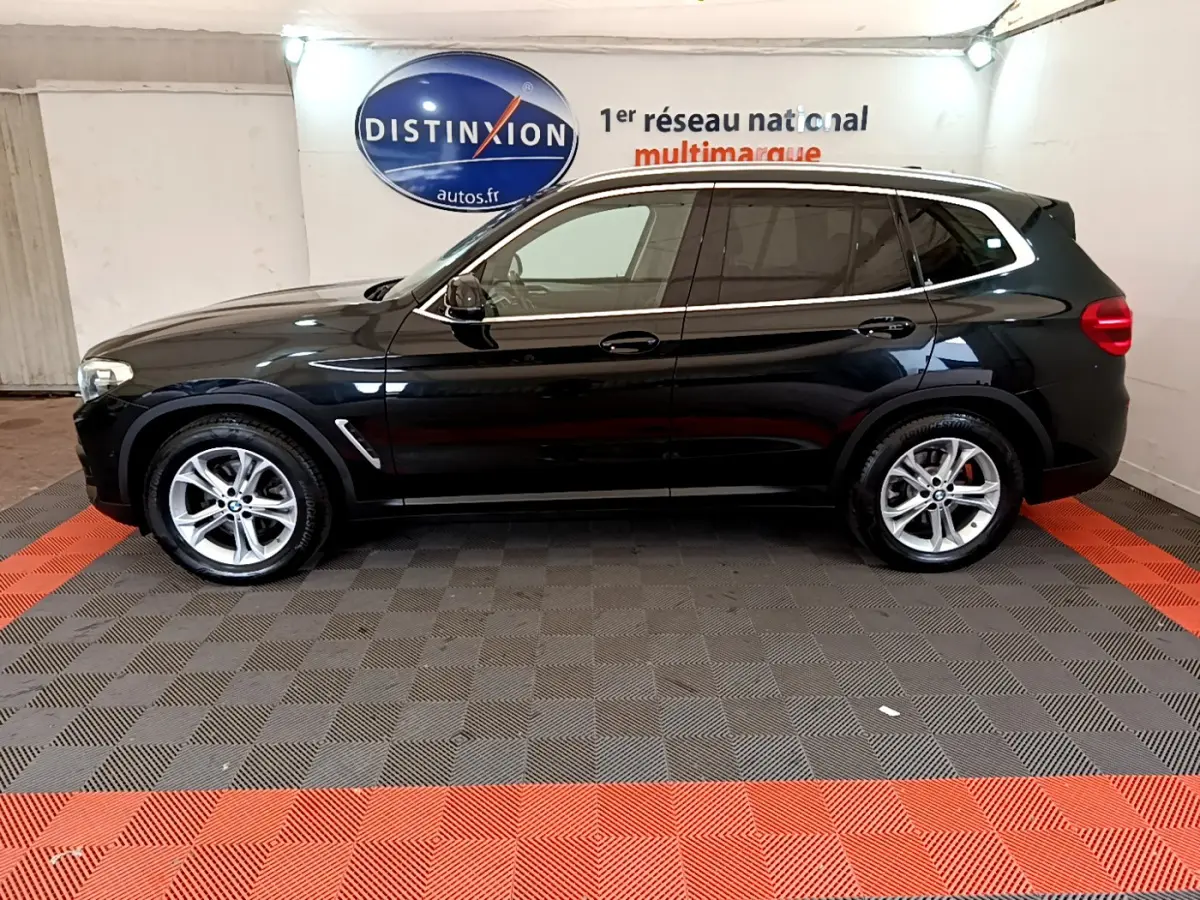 BMW X3 xDrive20d noir vue de profil côté gauche dans un showroom avec sol gris et bandes rouges.