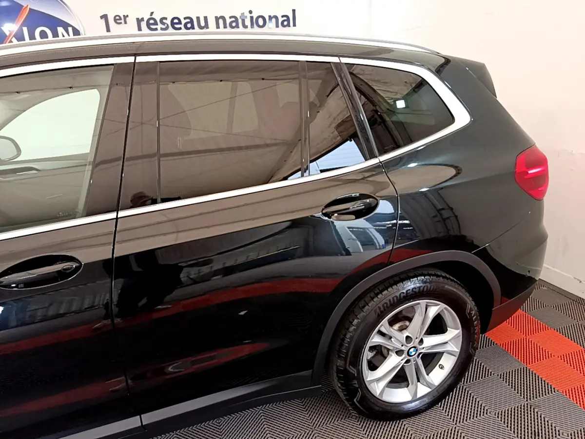 Vue latérale côté droit d'un BMW X3 noir avec jantes alliage et vitres teintées dans un showroom intérieur.