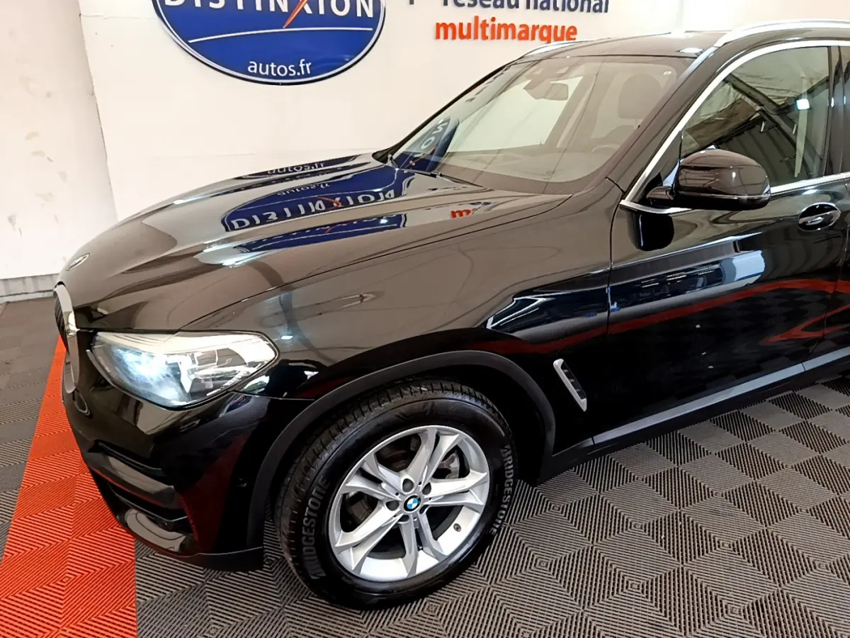 Vue 3/4 avant gauche d'un BMW X3 noir brillant avec jantes alliage et phares LED allumés.