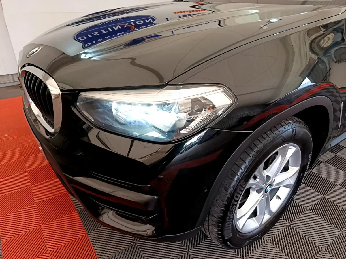 Gros plan sur l'avant droit noir d'un BMW X3 xDrive20d 2020 avec phare allumé et jante alu visible.