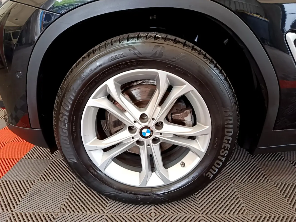 Gros plan sur la roue avant gauche noire d'un BMW X3 xDrive20d 2020 avec jante alliage et pneu Bridgestone.