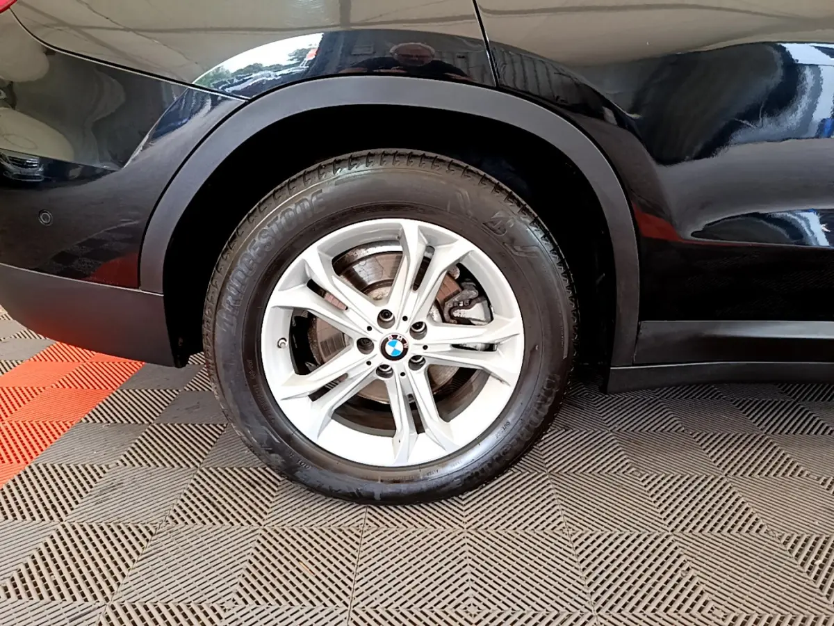 Gros plan sur la roue avant gauche d’un BMW X3 noir, avec jante alliage argent et logo BMW central.