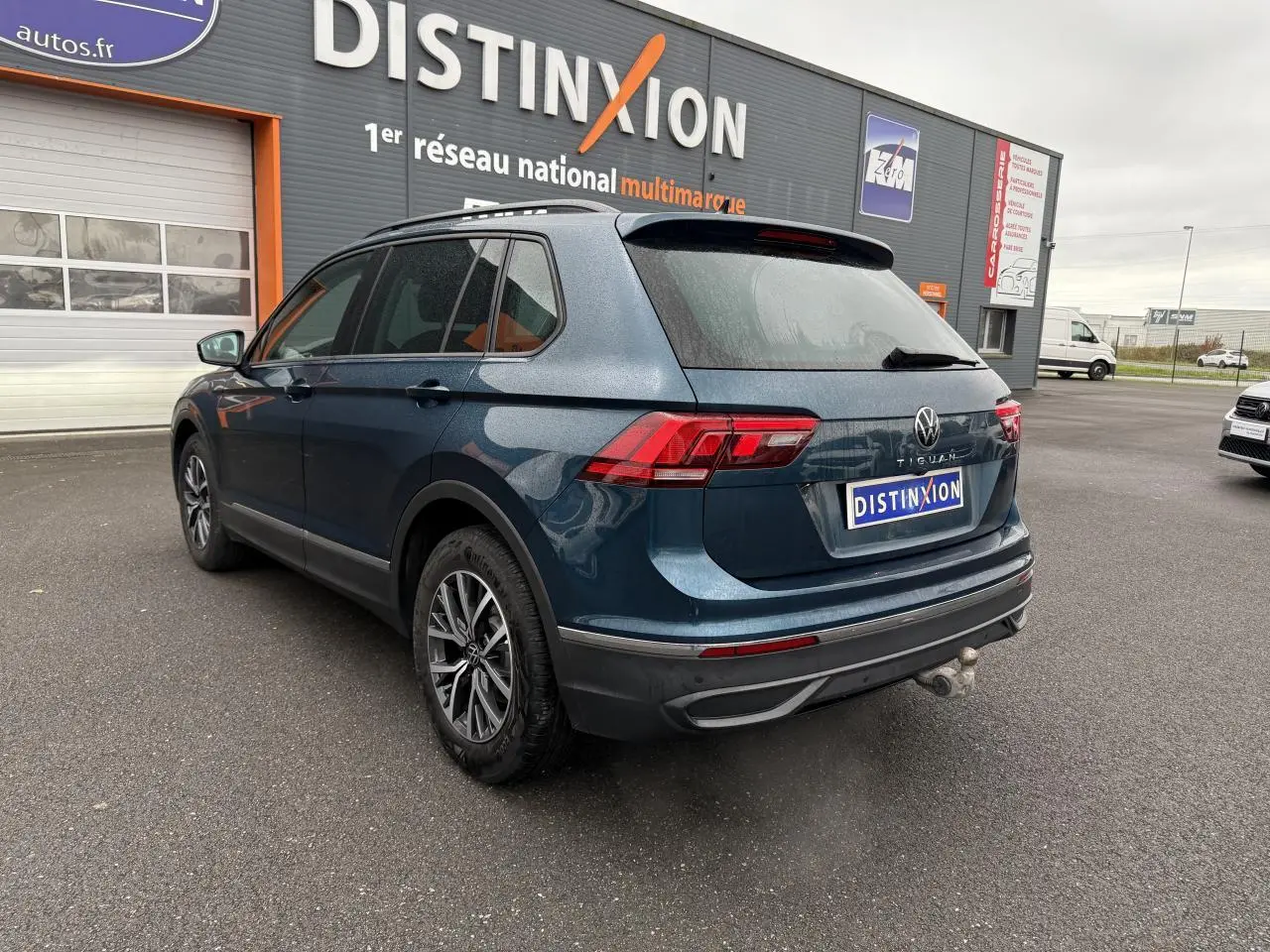 Vue 3/4 arrière gauche d'un Volkswagen Tiguan 2022 bleu Nightshade avec crochet d'attelage et jantes alliage 17 pouces.