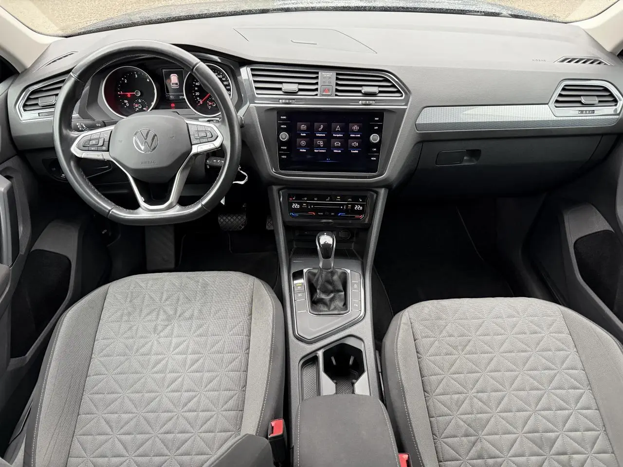 Vue intérieure du tableau de bord et des sièges gris tissu du Volkswagen Tiguan 2022 avec écran tactile central et volant multifonctions.