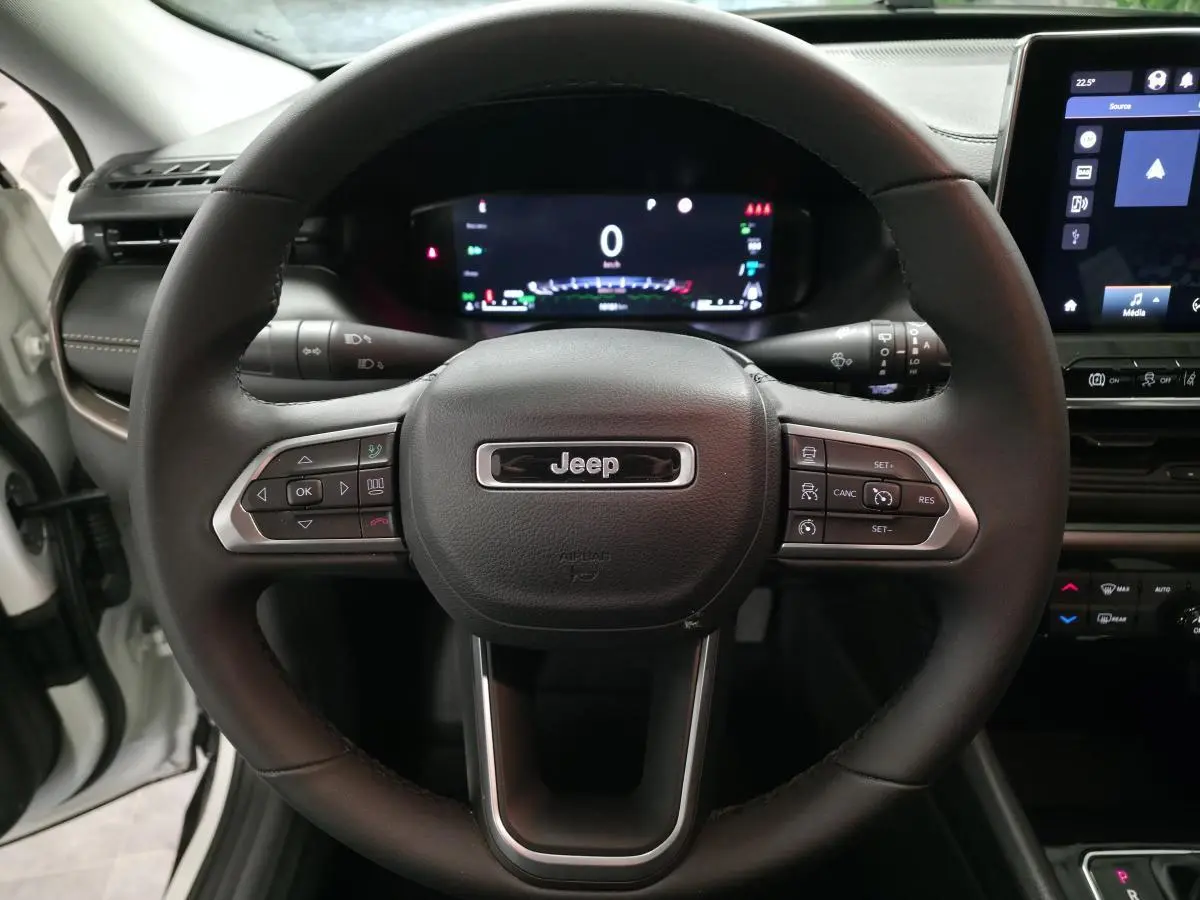 Vue rapprochée du volant Jeep Compass 2024 noir avec commandes intégrées et tableau de bord numérique allumé