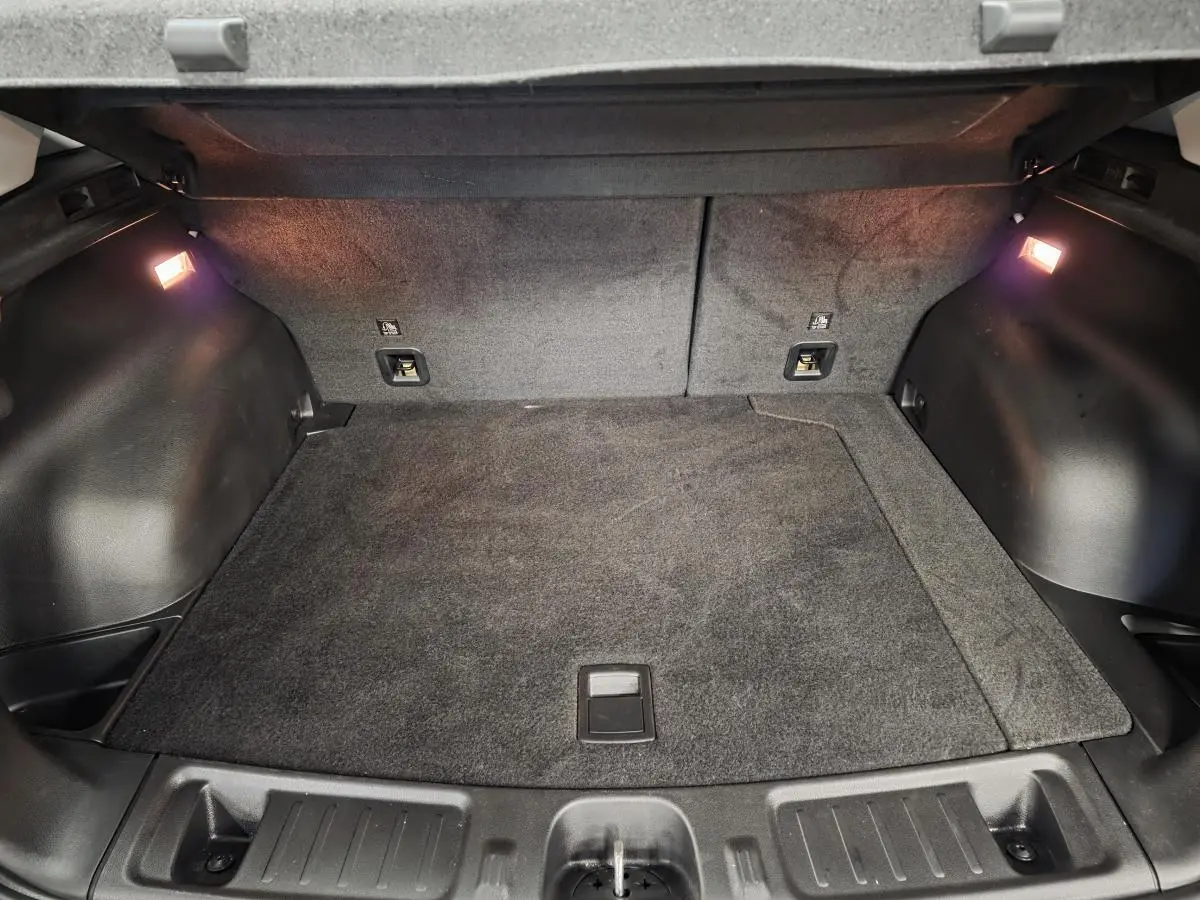 Coffre spacieux et éclairé du Jeep Compass blanc 2024, vue intérieure arrière avec tapis gris.