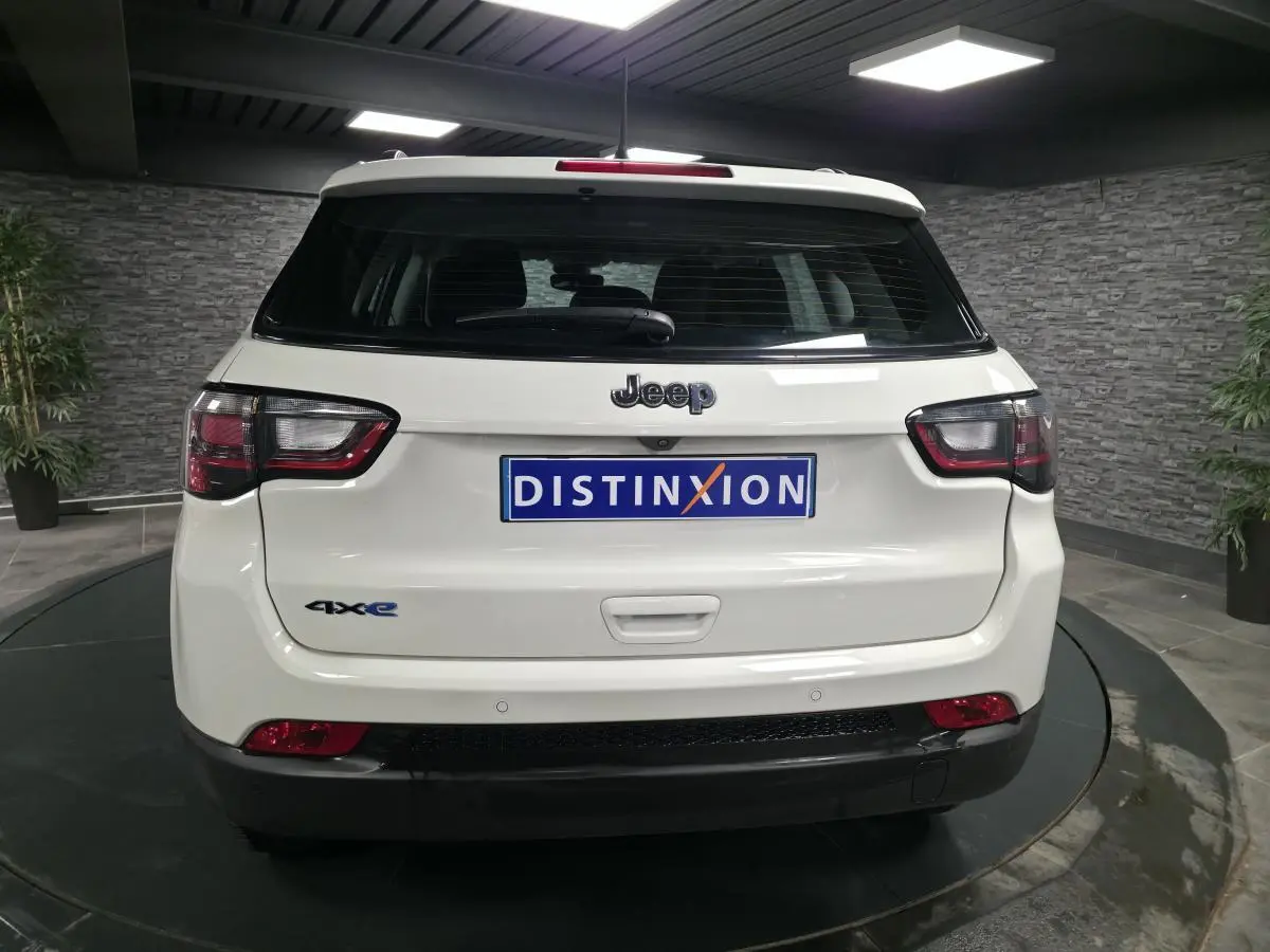 Vue arrière d'un Jeep Compass blanc hybride rechargeable avec logo 4xe et plaque Distinxion dans un showroom.