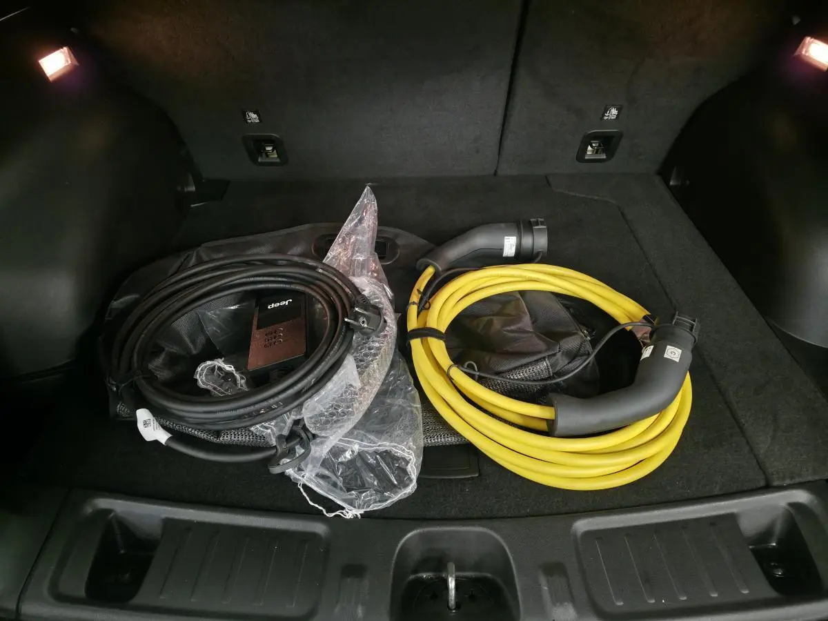 Coffre ouvert d'un Jeep Compass blanc 2024 montrant deux câbles de recharge, noir et jaune, sur tapis noir.