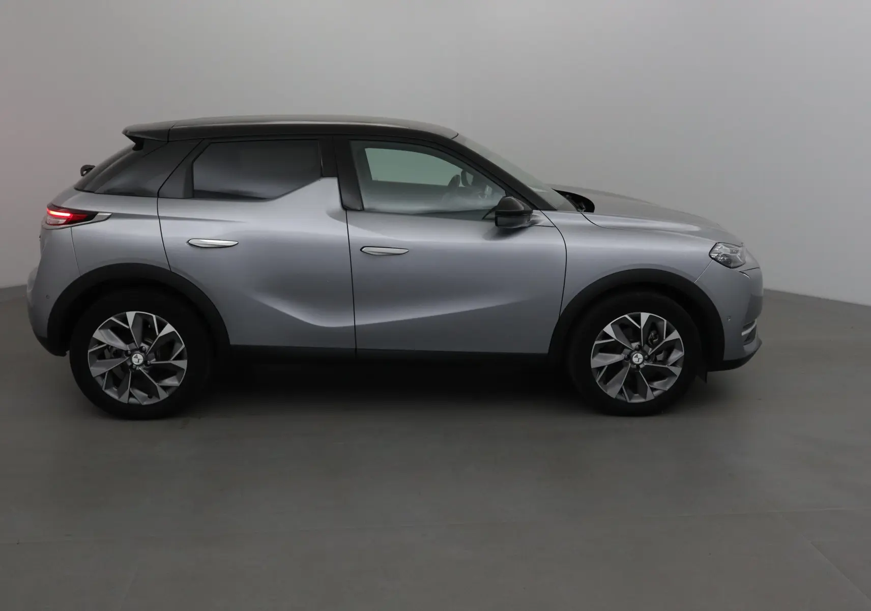 Vue de profil côté gauche du DS3 Crossback E-TENSE gris Artense avec toit noir et jantes stylisées.
