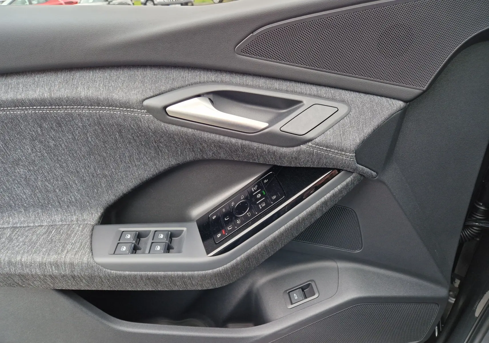 Gros plan sur la porte côté conducteur de l'Audi Q6 e-tron gris Manhattan, mettant en valeur les commandes électriques et le tissu texturé.