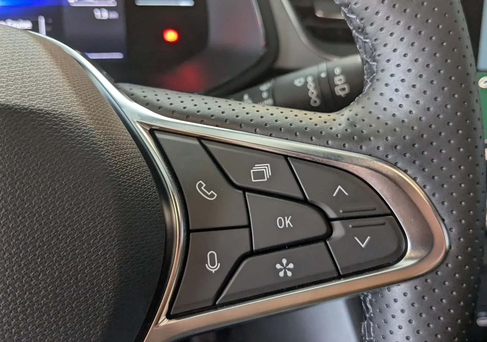 Gros plan sur les commandes du volant en cuir perforé du Renault Captur gris Cassiopée 2025, version hybride.