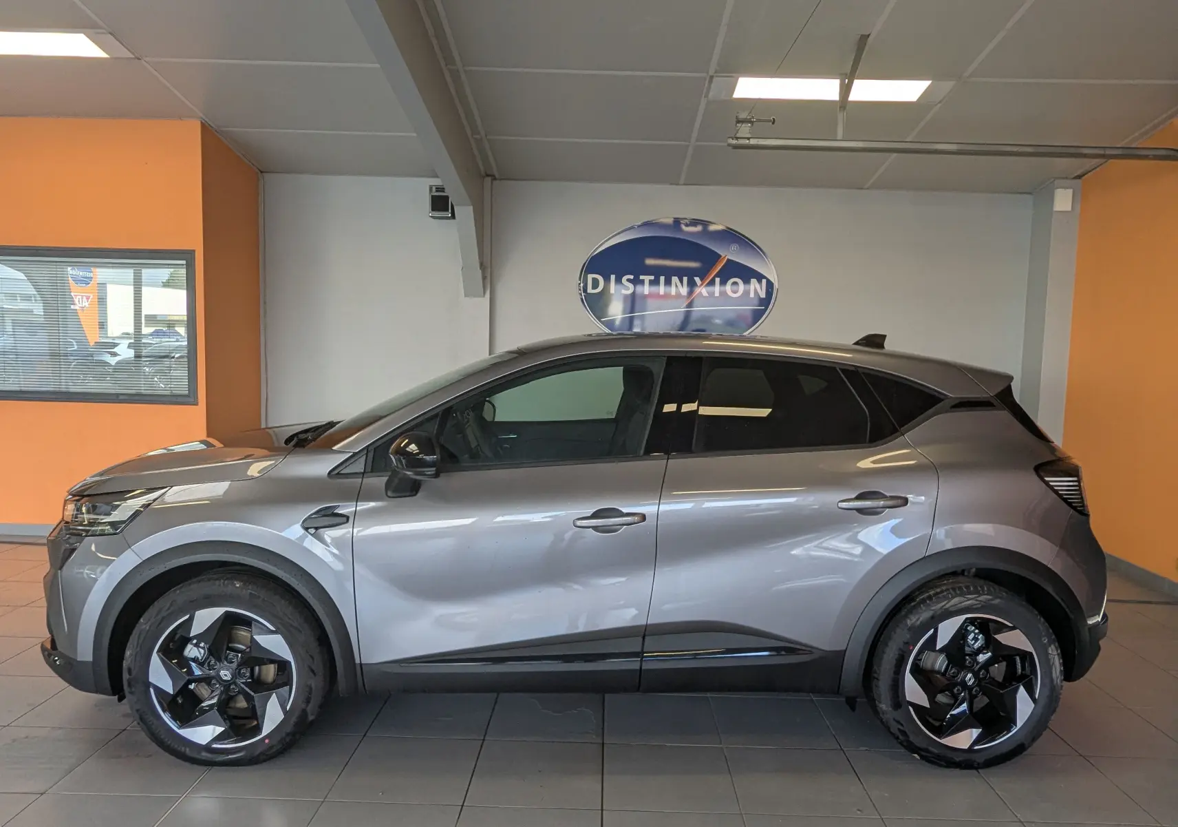 Profil côté gauche d'un Renault Captur E-Tech Full Hybrid 160ch gris Cassiopée avec jantes bicolores en intérieur showroom.