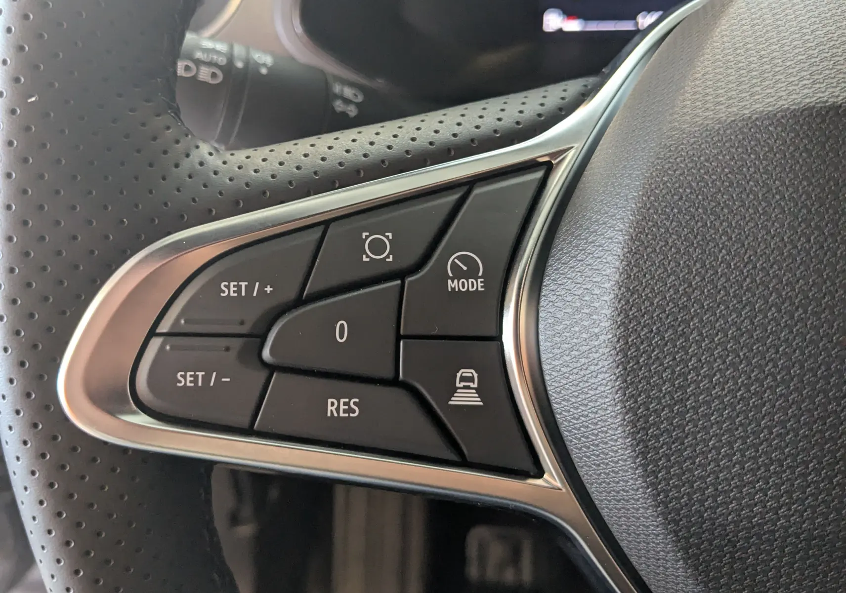 Gros plan sur les commandes du volant à gauche du Renault Captur gris Cassiopée 2025 hybride avec boutons de régulateur et mode conduite.