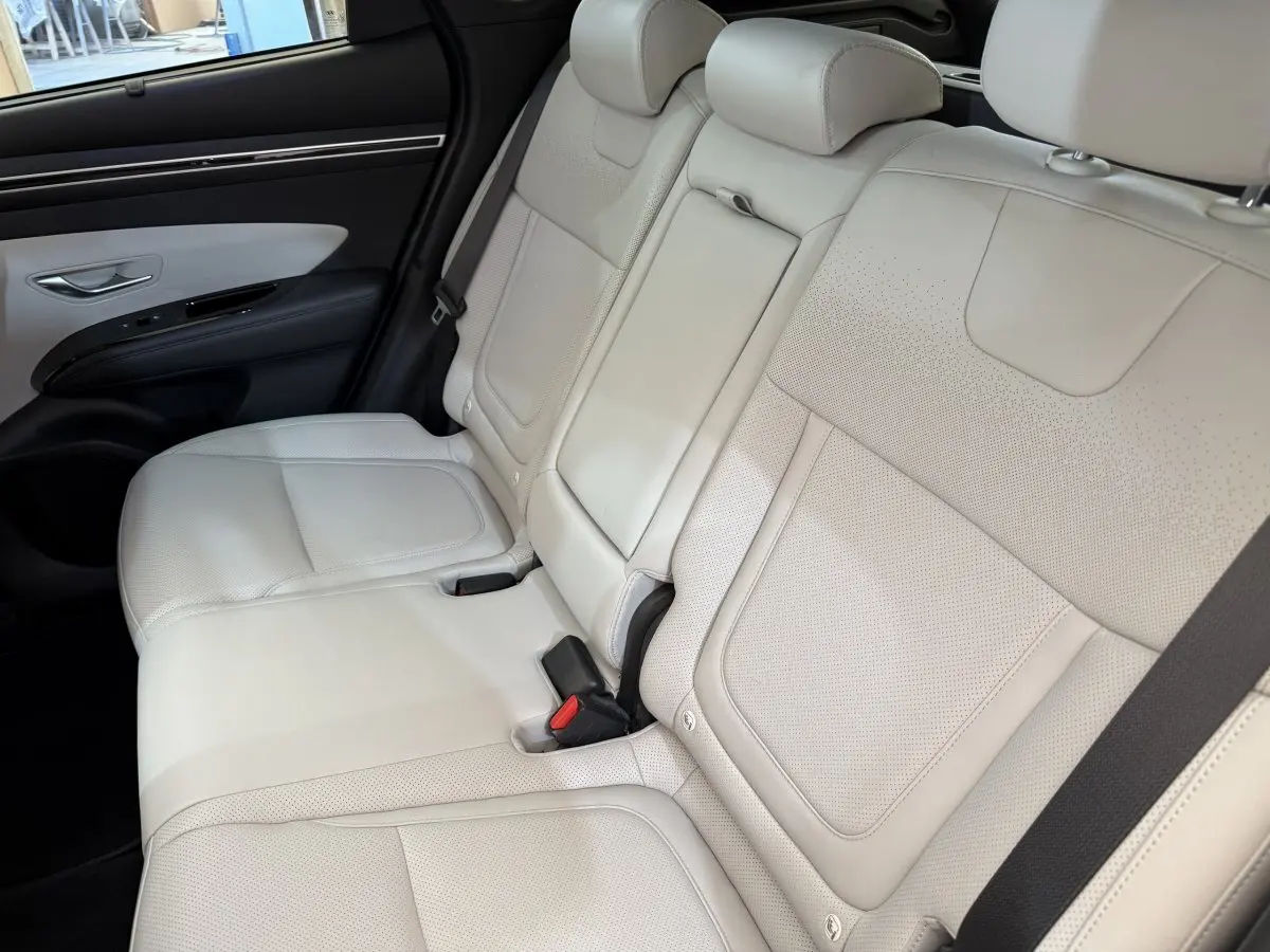 Vue latérale des sièges arrière en cuir beige clair du Hyundai Tucson 2022, avec ceinture de sécurité et porte noir.
