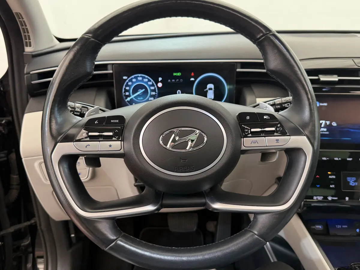 Vue rapprochée du volant cuir noir du Hyundai Tucson 2022 avec commandes multifonctions et tableau de bord digital.