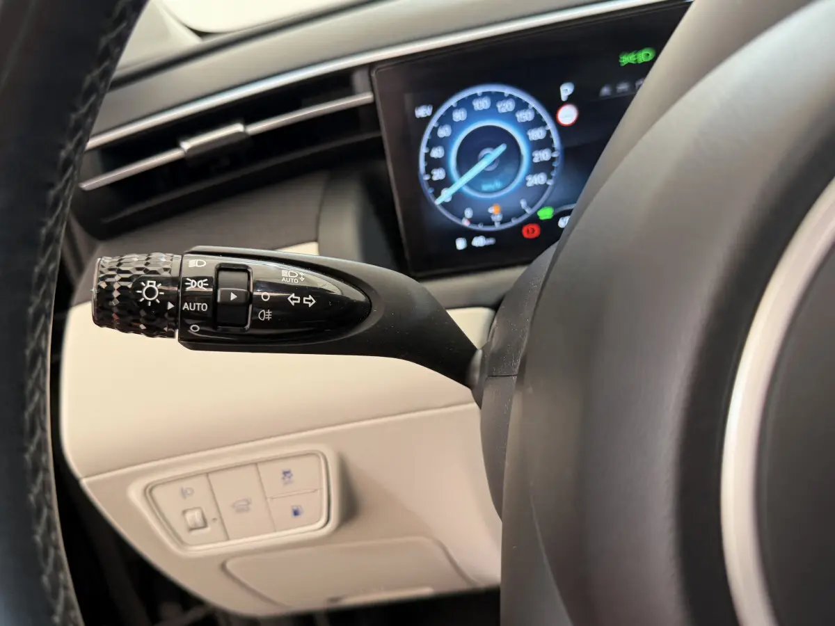 Gros plan sur la manette de feux et clignotants à gauche du volant d'un Hyundai Tucson noir, avec tableau de bord numérique visible.