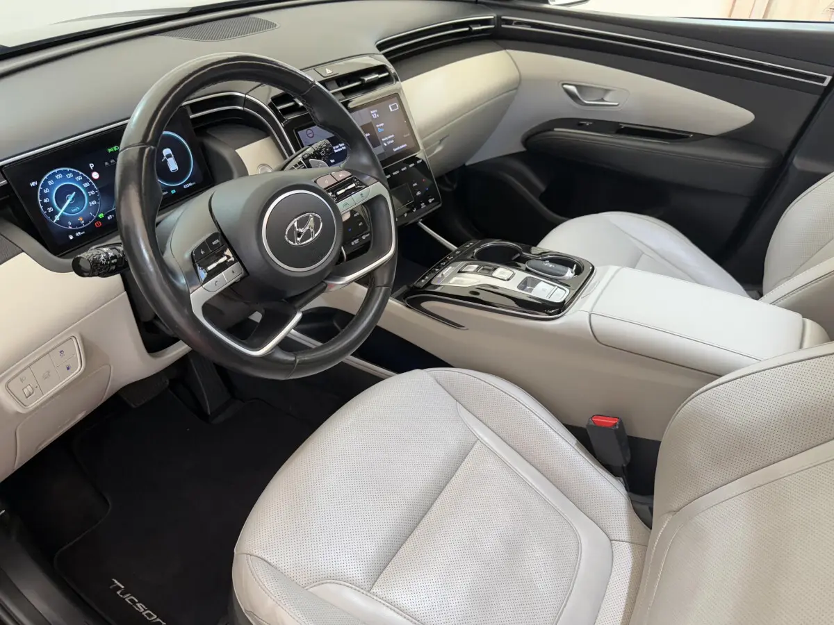 Intérieur clair du Hyundai Tucson 2022 vu côté conducteur, avec volant cuir et tableau de bord digital.