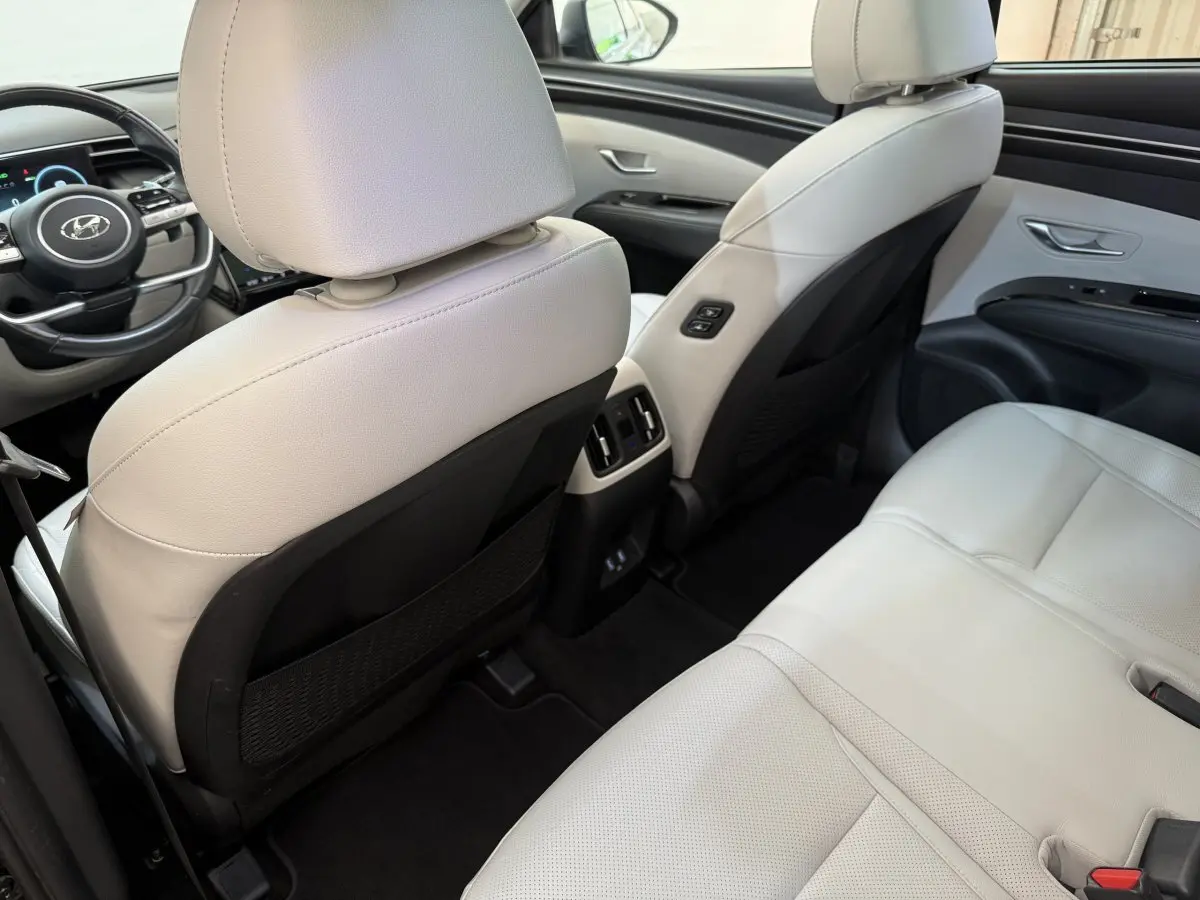 Vue arrière intérieure du Hyundai Tucson 2022 hybride rechargeable, sièges cuir blanc et console centrale avec aérateurs.