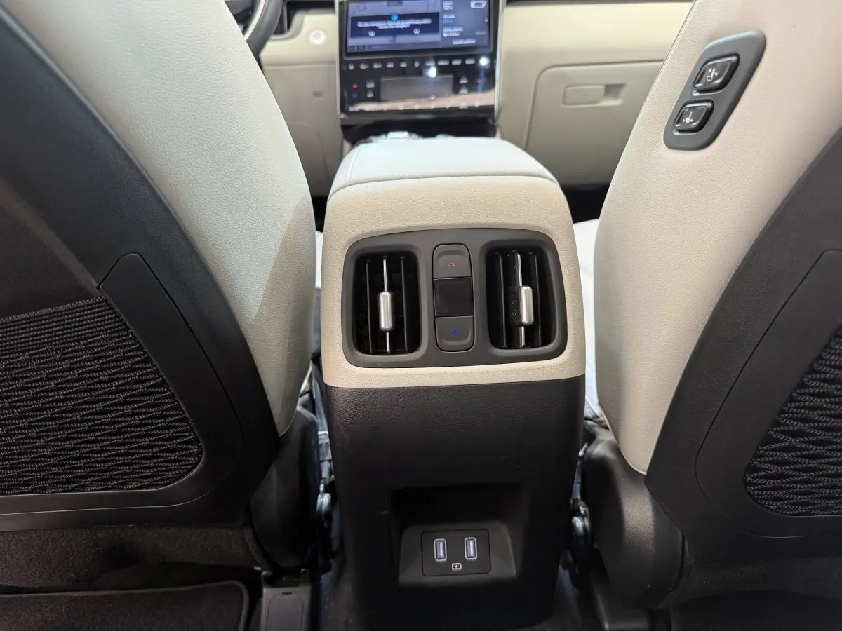 Vue rapprochée de la console centrale arrière beige et noire du Hyundai Tucson 1.6 PHEV avec commandes de climatisation et ports USB.