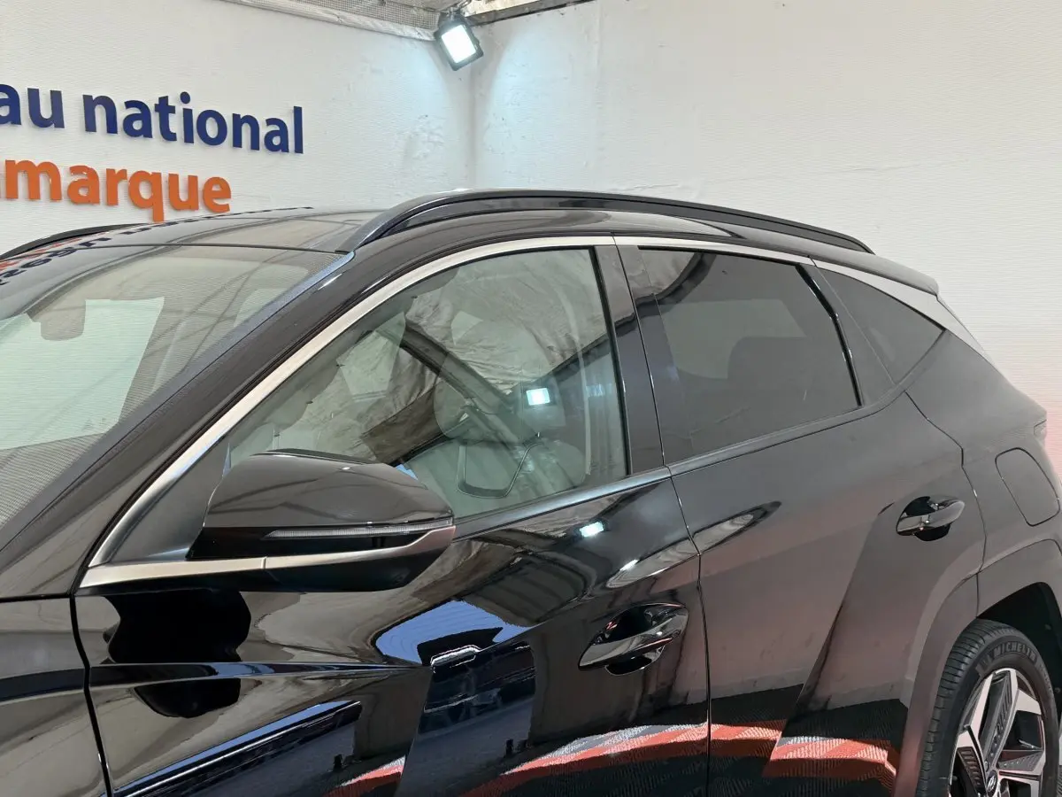 Profil côté gauche du Hyundai Tucson noir 2022 avec rétroviseur et poignées de porte visibles en intérieur showroom.