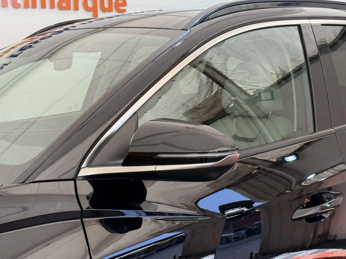 Gros plan sur le rétroviseur côté gauche d’un Hyundai Tucson noir brillant avec détails chromés et vitre avant visible.