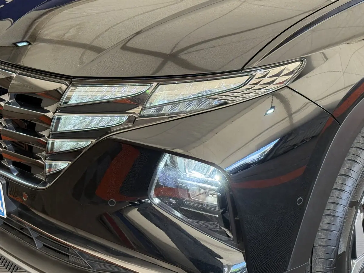 Gros plan sur l'avant droit noir brillant du Hyundai Tucson 2022, mettant en valeur ses phares LED et la calandre distinctive.