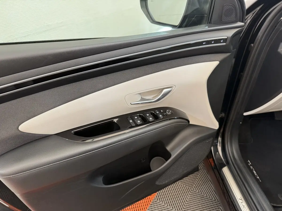 Intérieur côté gauche de la porte avant noire du Hyundai Tucson 2022 avec commandes électriques et garniture bicolore claire.