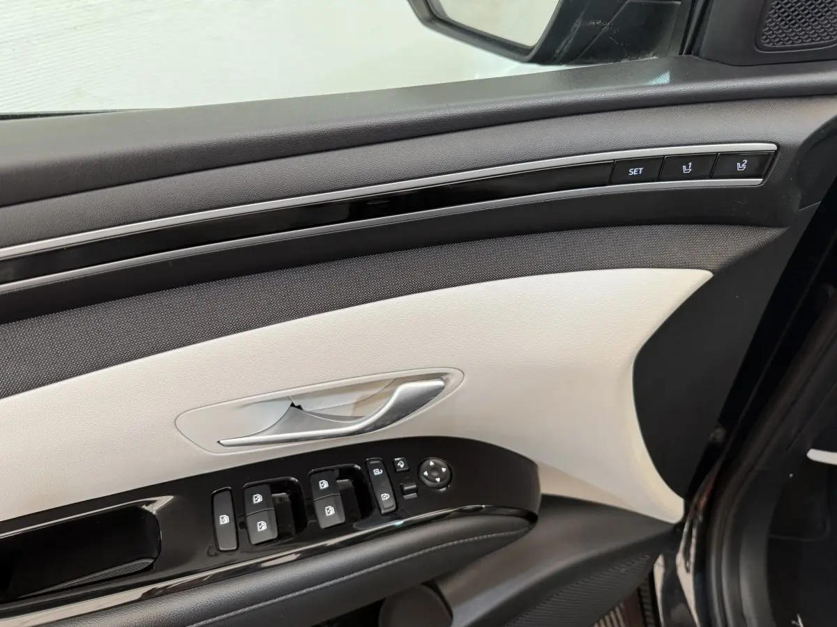 Intérieur côté conducteur du Hyundai Tucson noir 2022, panneau de porte beige et noir avec commandes électriques et réglages mémoire.