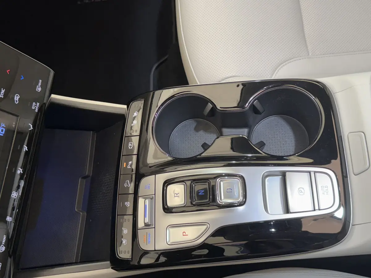 Gros plan sur la console centrale noire brillante du Hyundai Tucson 2022 avec commandes de boîte auto et porte-gobelets.