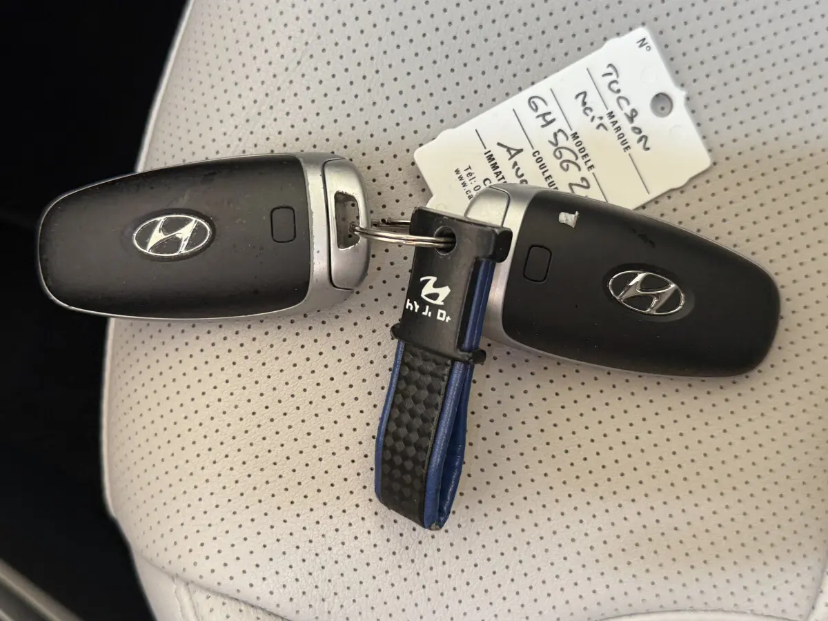 Gros plan sur deux clés noires Hyundai Tucson posées sur un siège en cuir perforé beige avec étiquette d'identification.