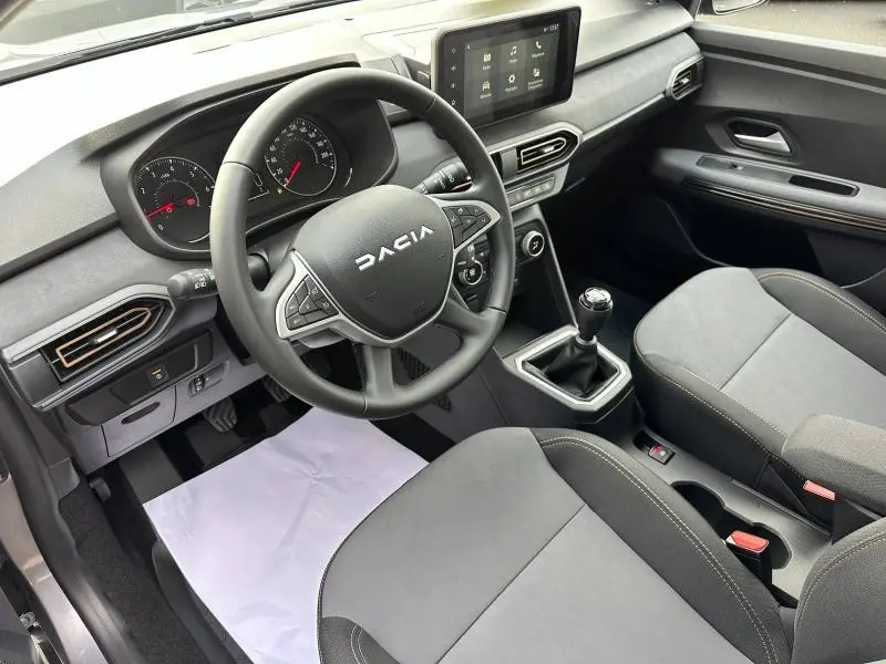 Intérieur de la Dacia Sandero 2025 en gris, vue côté conducteur montrant volant, tableau de bord et levier de vitesses manuel.