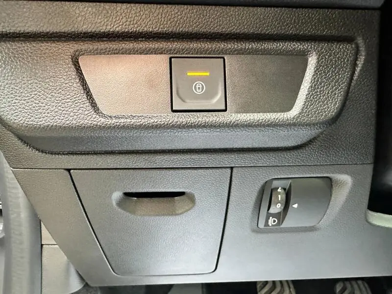 Gros plan sur le bouton de verrouillage central et le réglage des phares du tableau de bord d'une Dacia Sandero Stepway gris schiste.