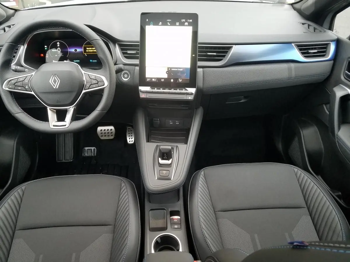 Vue intérieure avant du Renault Captur 2025, tableau de bord moderne avec écran tactile vertical et sièges noirs.