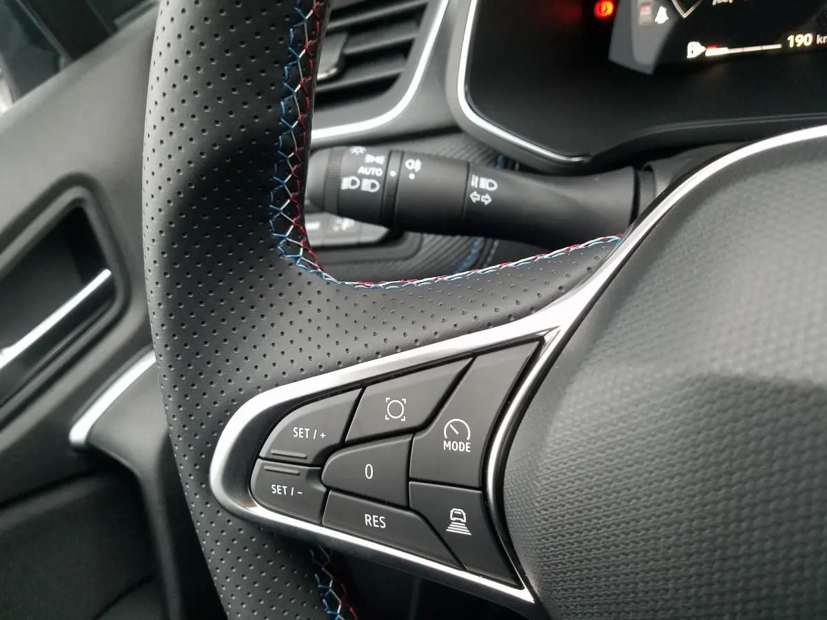 Gros plan sur le volant perforé du Renault Captur gris Rafale, mettant en valeur les commandes de régulateur adaptatif.