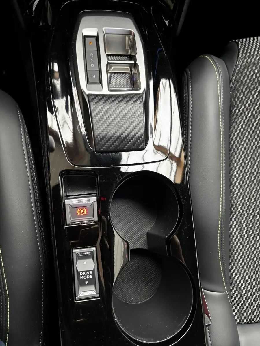 Vue rapprochée de la console centrale noire brillante de la Peugeot 208 Hybrid 110 e-DCS6 GT avec levier de vitesses et porte-gobelets.