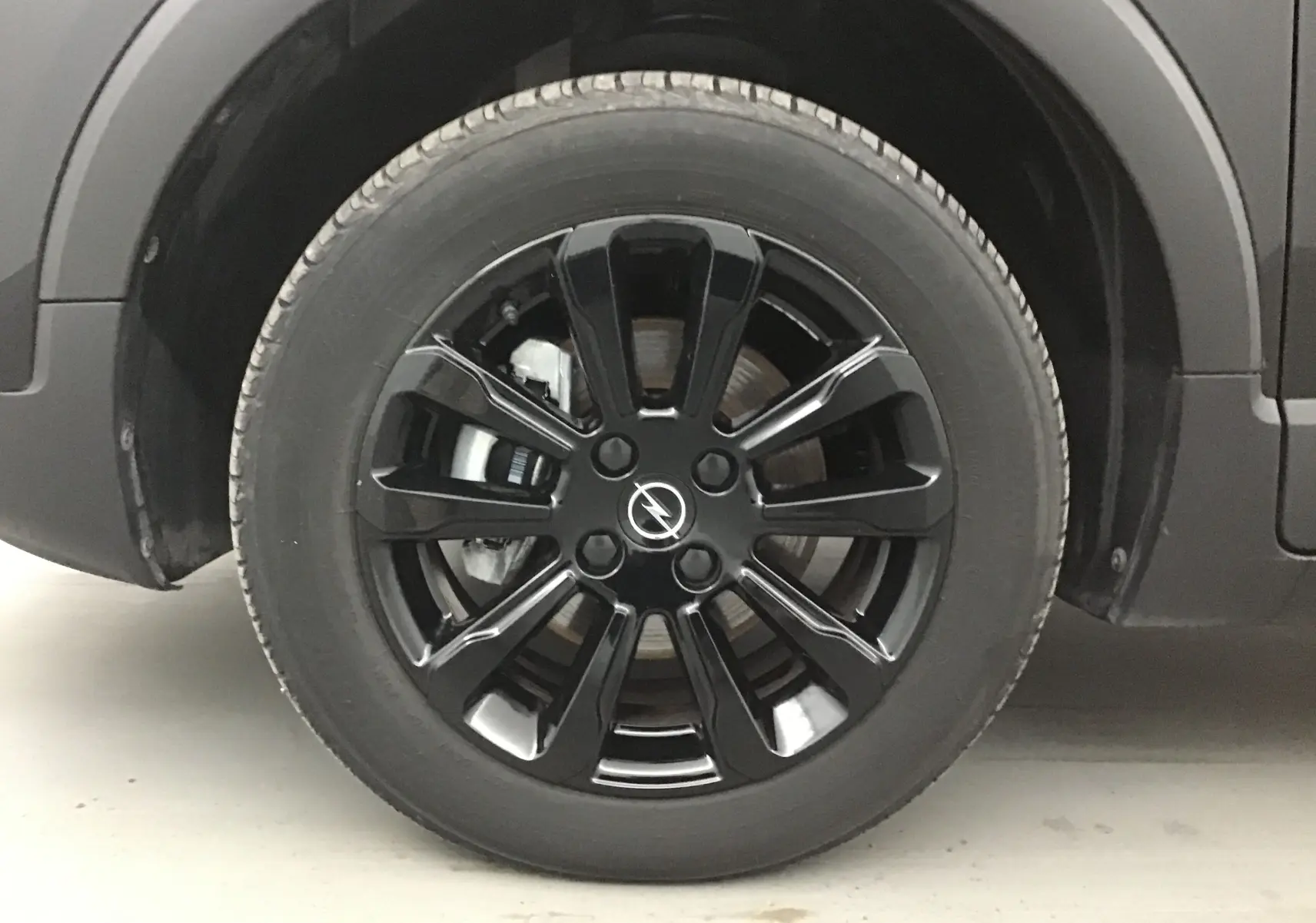 Gros plan sur la roue avant gauche noire d'un Opel Crossland 2022 avec jante alliage noire brillante et logo Opel central.