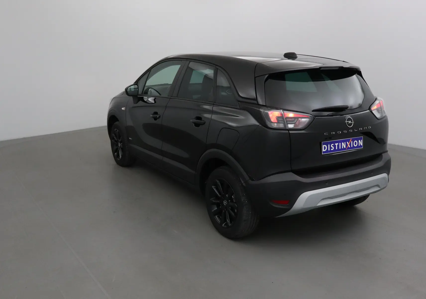 Opel Crossland noir vue 3/4 arrière droit, avec jantes noires et feux arrière allumés dans un studio.