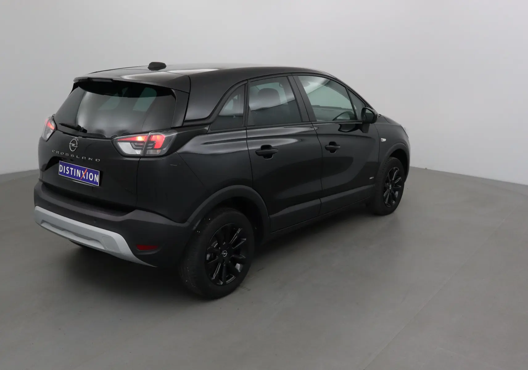 Opel Crossland noir vue 3/4 arrière droit, avec jantes noires et feux arrière allumés dans un studio.