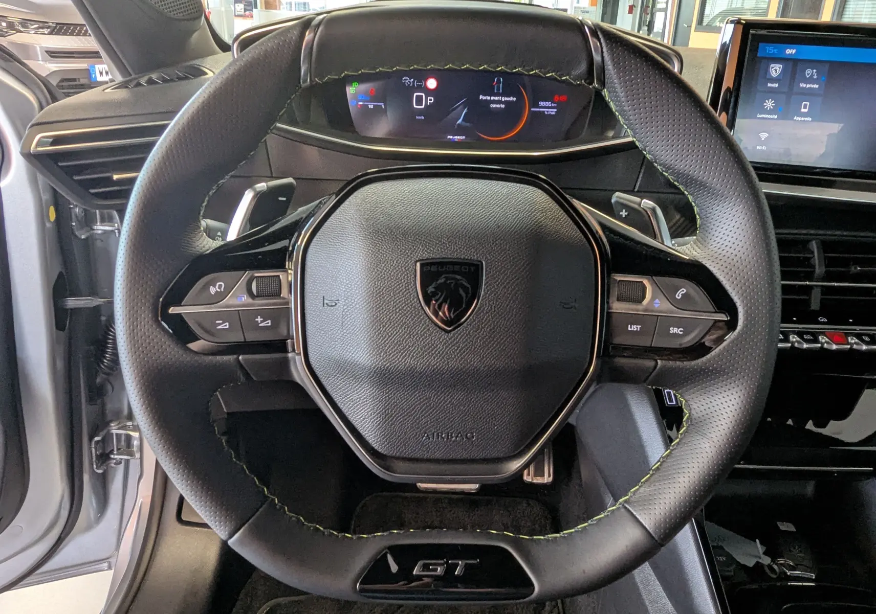 Vue rapprochée du volant GT noir avec surpiqûres vertes et tableau de bord numérique d'une Peugeot 208 Gris Artens 2024.