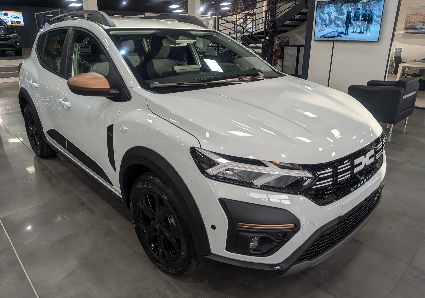 Vue 3/4 avant gauche d'une Dacia Sandero Stepway TCe 110 blanche avec rétroviseurs bronze et jantes noires en showroom.