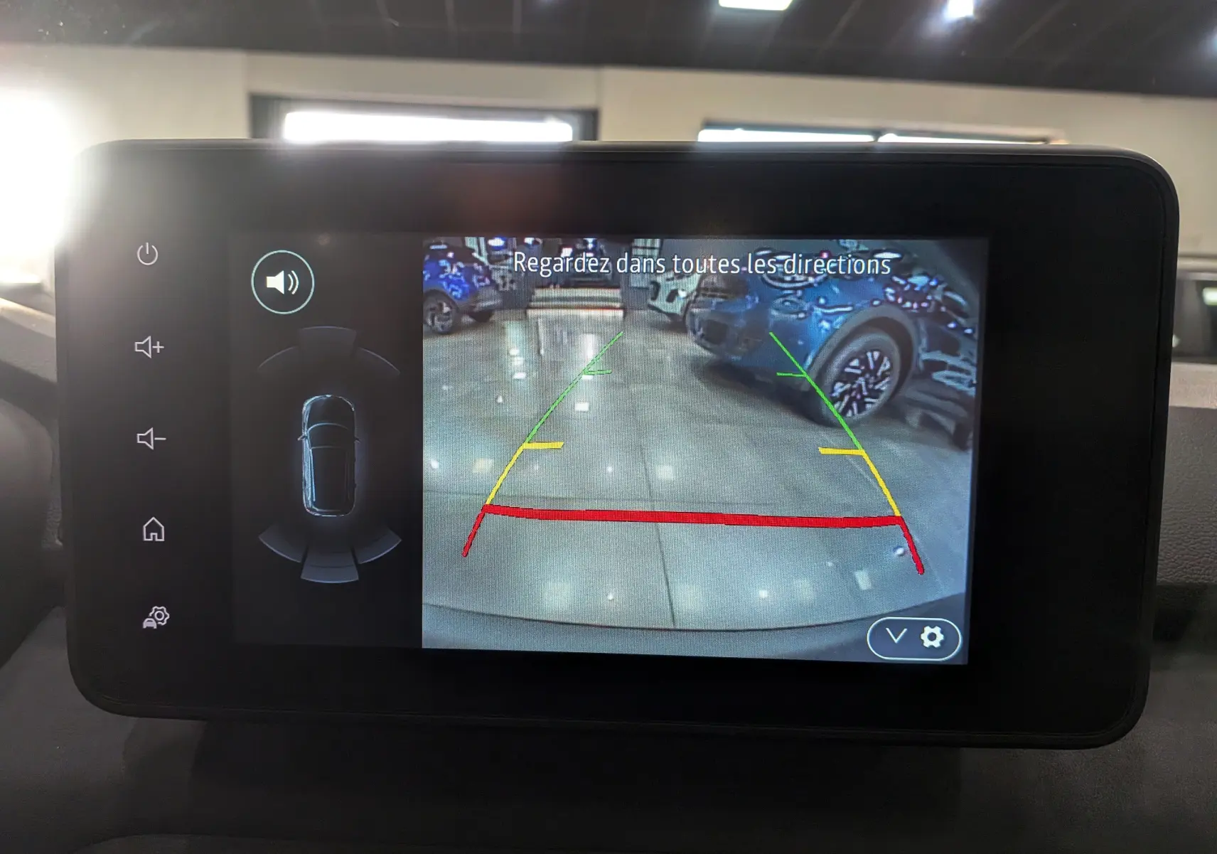 Écran de caméra de recul affichant l'arrière du Dacia Sandero Stepway blanc glacier en intérieur showroom.