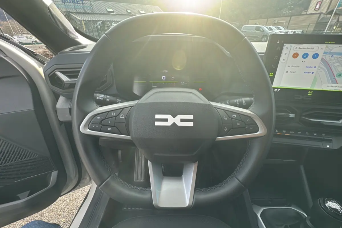 Vue intérieure centrée sur le volant cuir du Dacia Duster TCE 130 4x2 Journey 2025 avec écran tactile et levier de vitesse manuel.