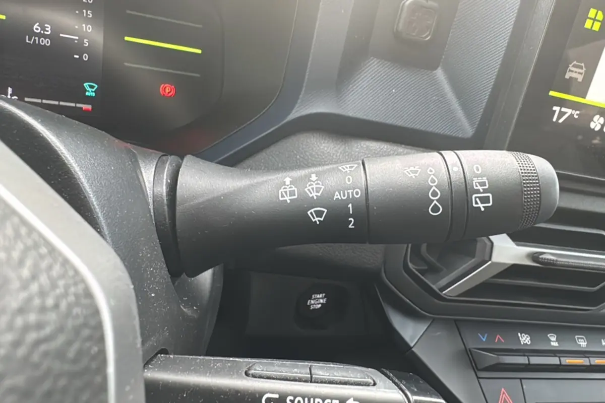 Gros plan sur la commande d’essuie-glace du Dacia Duster 2025, intérieur noir avec tableau de bord numérique.