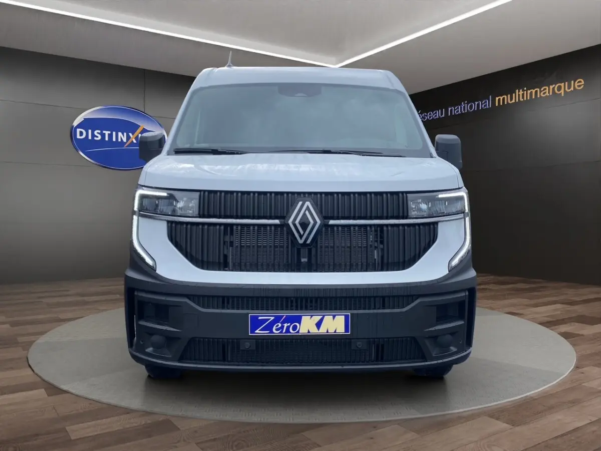 Vue frontale d’un Renault Master blanc avec calandre noire et phares LED, sur fond intérieur showroom multimarque.