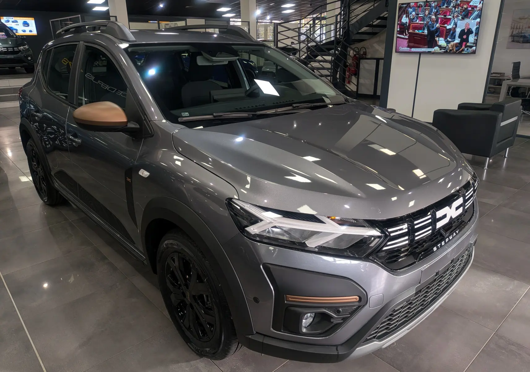 Vue 3/4 avant droite d'une Dacia Sandero Stepway TCe 110 gris schiste avec rétroviseurs bronze et jantes noires en showroom.